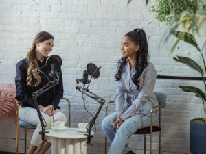 Deux femmes souriantes en train de faire un podcast assises sur des chaises