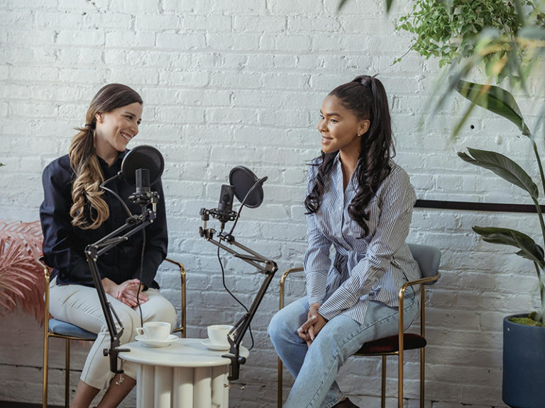 Deux femmes souriantes en train de faire un podcast assises sur des chaises